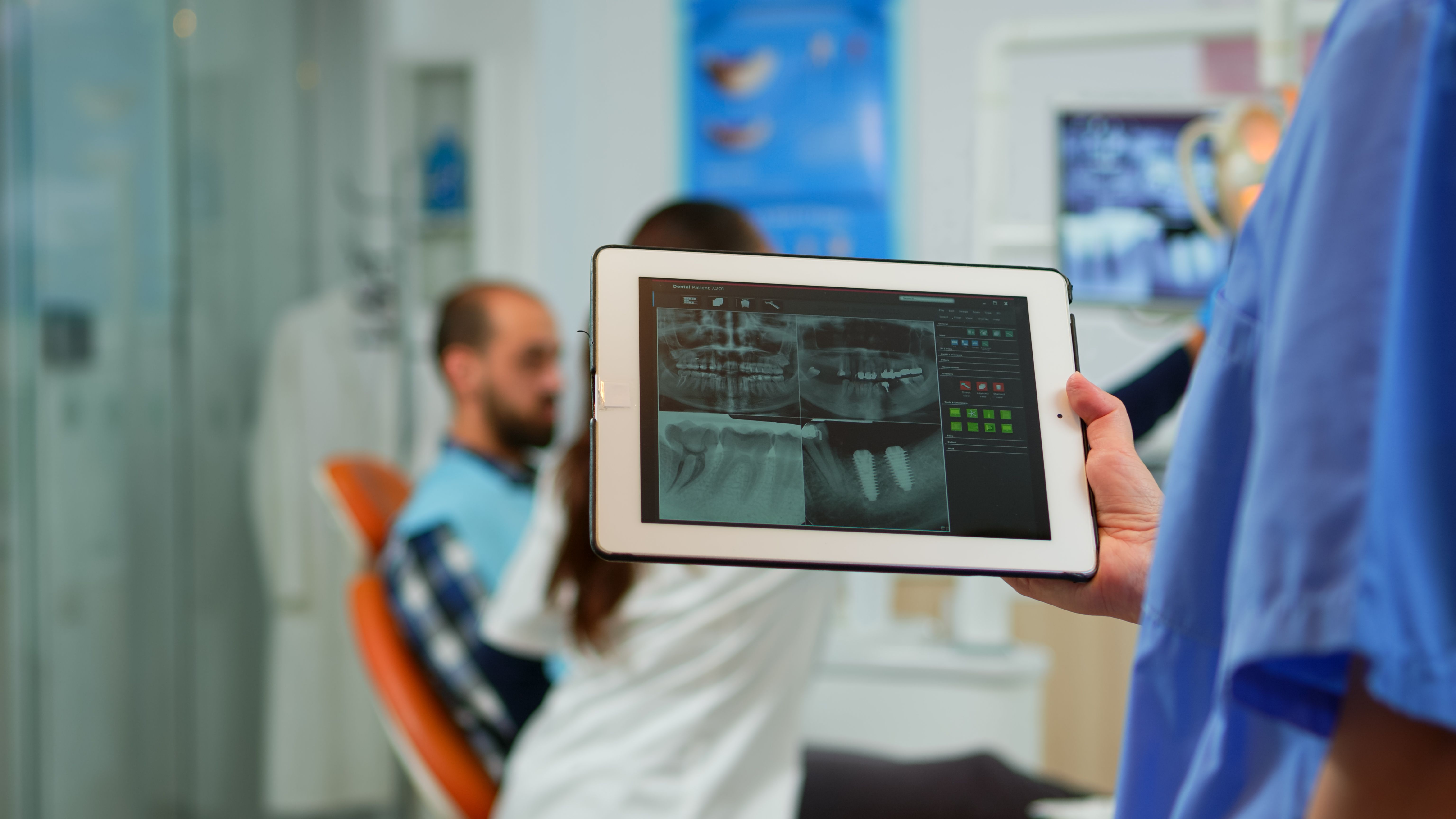 close-up-dentist-nurse-holding-tablet-with-digital-radiography-while-doctor-is-working-with-patient-background-examining-teeth-problem-sitting-stomatological-chair-dental-clinic